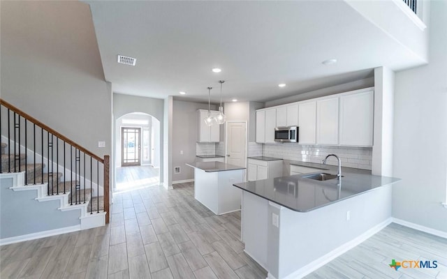 kitchen with white cabinetry, kitchen peninsula, sink, and hanging light fixtures