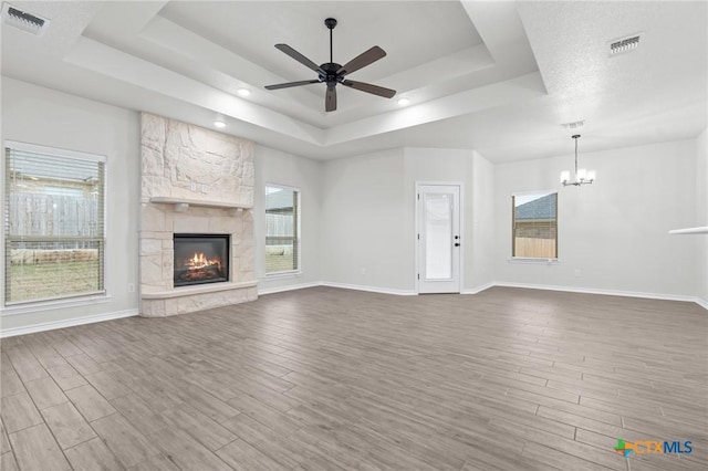 unfurnished living room with a healthy amount of sunlight, wood-type flooring, a tray ceiling, and a stone fireplace