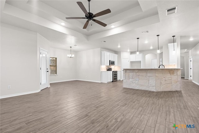 unfurnished living room featuring hardwood / wood-style flooring, a raised ceiling, and ceiling fan with notable chandelier