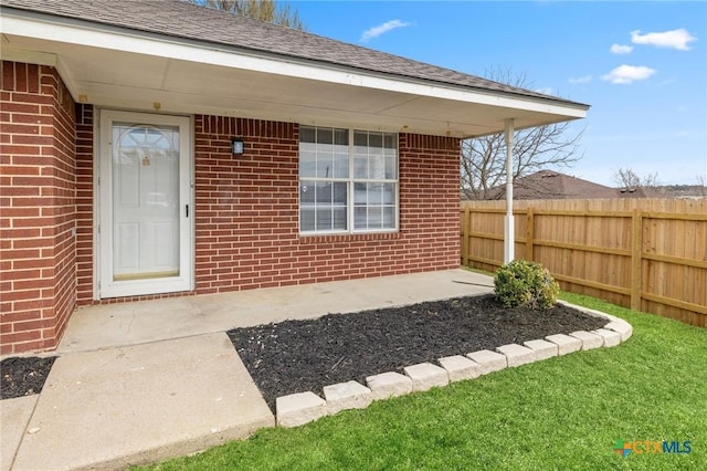 entrance to property with fence, brick siding, and roof with shingles