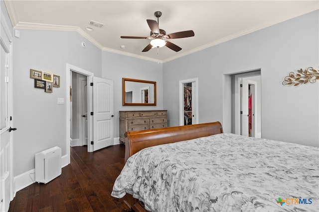 bedroom featuring a closet, a walk in closet, ornamental molding, dark hardwood / wood-style floors, and ceiling fan