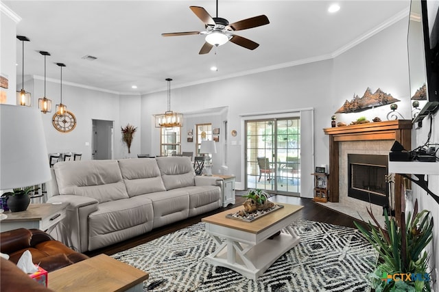 living room featuring ceiling fan with notable chandelier, dark wood-type flooring, crown molding, and a tile fireplace