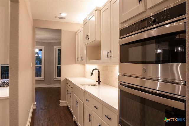 kitchen with sink, tasteful backsplash, white cabinetry, dark hardwood / wood-style floors, and double oven