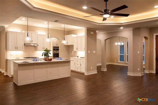 kitchen featuring decorative light fixtures, dark hardwood / wood-style floors, a raised ceiling, a kitchen island with sink, and white cabinets