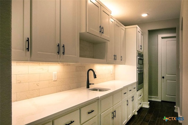 kitchen with white cabinetry, sink, decorative backsplash, and double oven