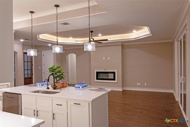 kitchen with a raised ceiling, an island with sink, sink, and white cabinetry