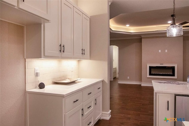 kitchen with dark wood-type flooring, crown molding, a raised ceiling, white cabinets, and backsplash