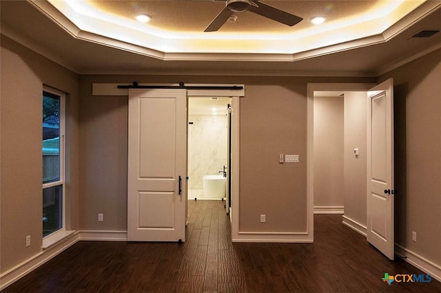 unfurnished bedroom with a barn door, dark hardwood / wood-style floors, and a tray ceiling