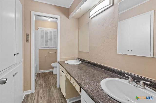 bathroom with toilet, double vanity, a sink, and wood finished floors