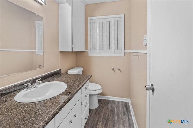 half bath with baseboards, wood finished floors, toilet, and vanity