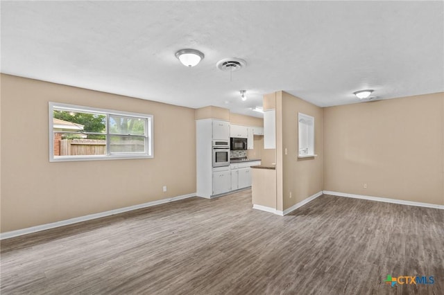 unfurnished living room featuring visible vents, baseboards, and dark wood-type flooring