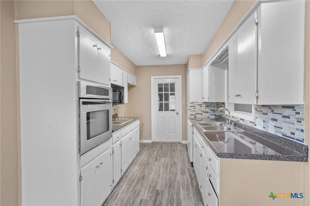 kitchen featuring black appliances, decorative backsplash, light wood finished floors, and a sink