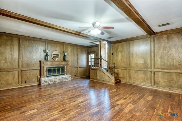 unfurnished living room with wood walls, beamed ceiling, dark hardwood / wood-style floors, ceiling fan, and a fireplace