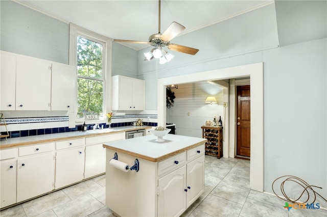 kitchen with a center island, white cabinets, sink, light tile patterned floors, and backsplash