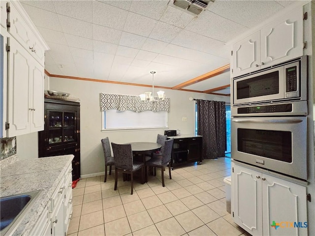 kitchen with sink, light tile patterned floors, stainless steel appliances, white cabinets, and decorative light fixtures