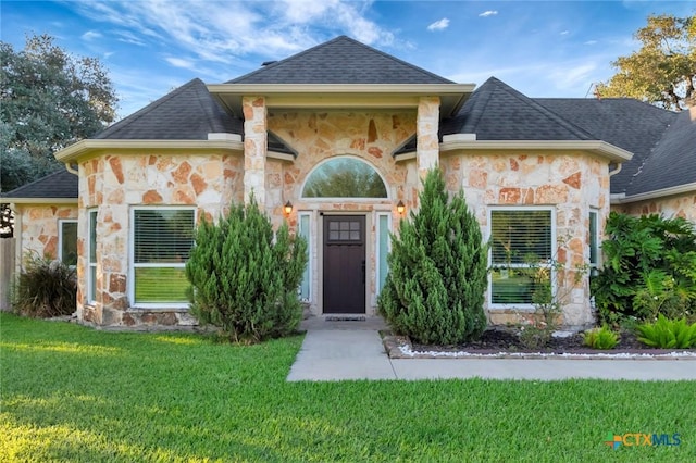 french country style house with stone siding, roof with shingles, and a front yard