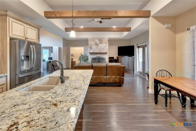 kitchen with stainless steel fridge, open floor plan, decorative light fixtures, light stone countertops, and a sink