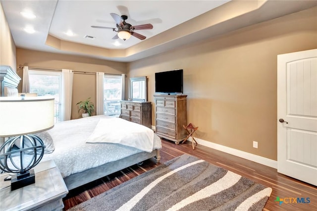 bedroom featuring ceiling fan, dark wood-type flooring, visible vents, baseboards, and a tray ceiling