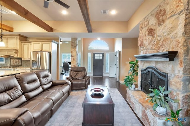 living area with ceiling fan, a fireplace, visible vents, and beam ceiling