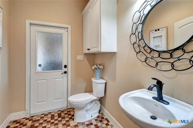 half bathroom with tile patterned floors, a sink, toilet, and baseboards