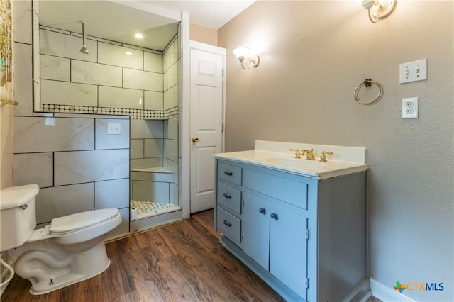 bathroom with hardwood / wood-style flooring, vanity, toilet, and tiled shower