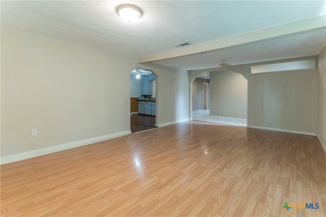 unfurnished room with a textured ceiling, light wood-type flooring, and ceiling fan