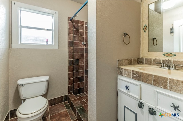 bathroom featuring tile patterned flooring, a tile shower, vanity, and toilet