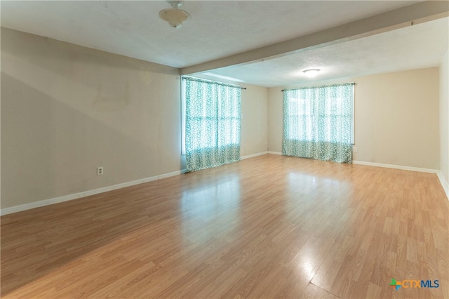 spare room with light hardwood / wood-style flooring and beamed ceiling