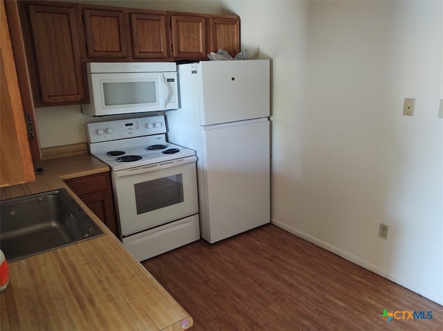 kitchen featuring dark wood-type flooring, white appliances, and sink