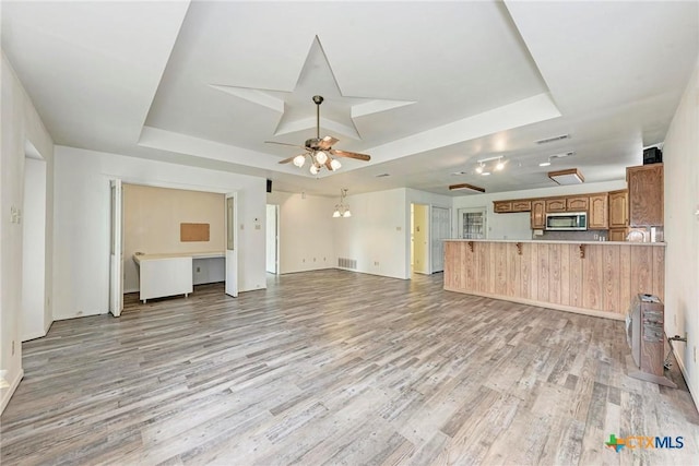 unfurnished living room with a raised ceiling, ceiling fan, and light hardwood / wood-style flooring