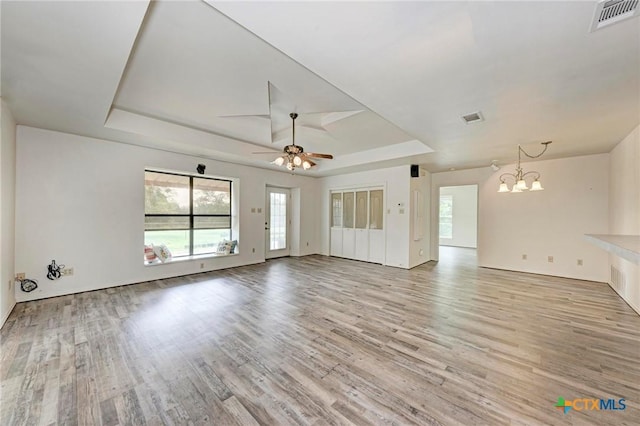 unfurnished living room with a tray ceiling, ceiling fan with notable chandelier, and light wood-type flooring