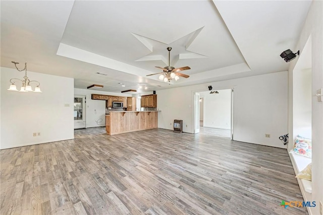 unfurnished living room featuring a tray ceiling, ceiling fan with notable chandelier, and light wood-type flooring