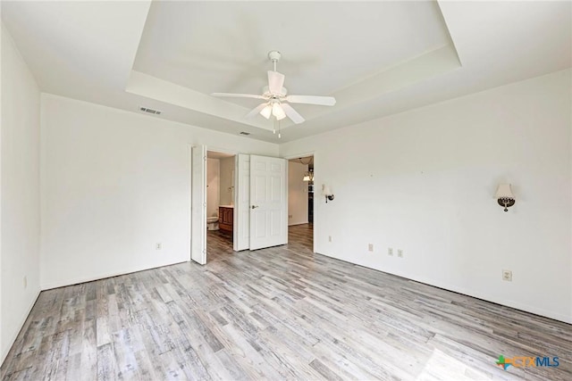 unfurnished bedroom with light hardwood / wood-style flooring, a raised ceiling, ceiling fan, and ensuite bathroom