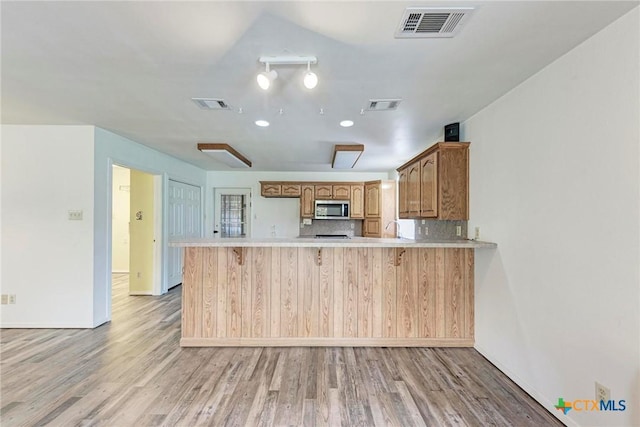 kitchen featuring sink, a breakfast bar area, backsplash, kitchen peninsula, and light wood-type flooring