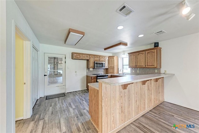 kitchen featuring range with electric cooktop, backsplash, light hardwood / wood-style floors, and kitchen peninsula