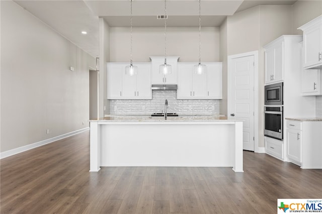 kitchen featuring stainless steel appliances, a towering ceiling, pendant lighting, an island with sink, and white cabinets