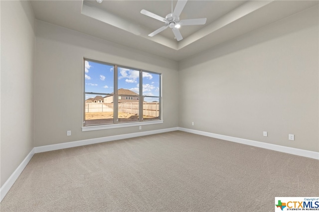 carpeted empty room featuring ceiling fan and a raised ceiling