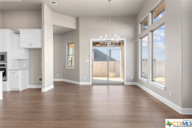 unfurnished dining area featuring a wealth of natural light, dark hardwood / wood-style flooring, and a notable chandelier