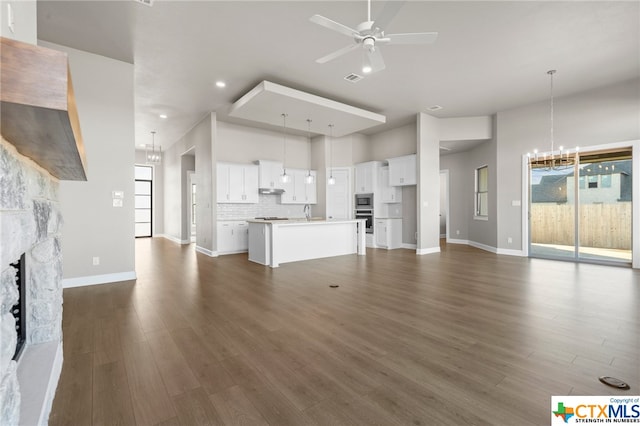 unfurnished living room with a fireplace, ceiling fan with notable chandelier, sink, and dark hardwood / wood-style flooring