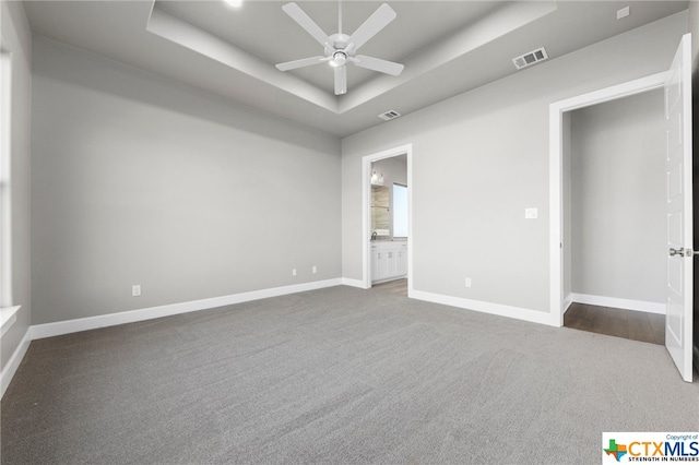 unfurnished bedroom featuring ensuite bathroom, ceiling fan, and a raised ceiling