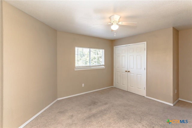 unfurnished bedroom featuring a closet, a textured ceiling, light carpet, and ceiling fan