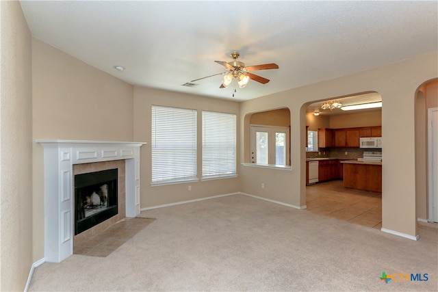 unfurnished living room featuring a tile fireplace, light colored carpet, and ceiling fan