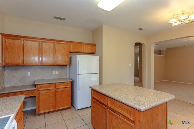 kitchen featuring backsplash, white appliances, light tile patterned floors, and a center island