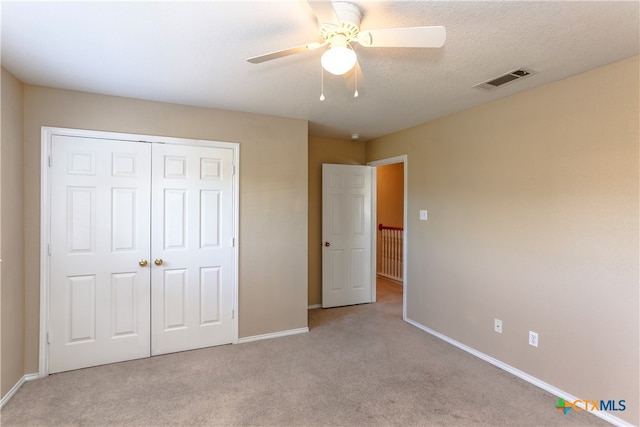 unfurnished bedroom featuring ceiling fan, a textured ceiling, a closet, and light colored carpet