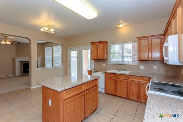 kitchen featuring sink, light tile patterned floors, a fireplace, white appliances, and a kitchen island