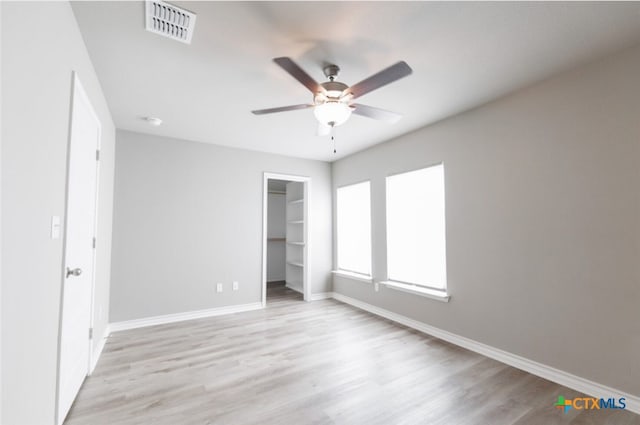 unfurnished bedroom featuring a closet, a walk in closet, light hardwood / wood-style floors, and ceiling fan