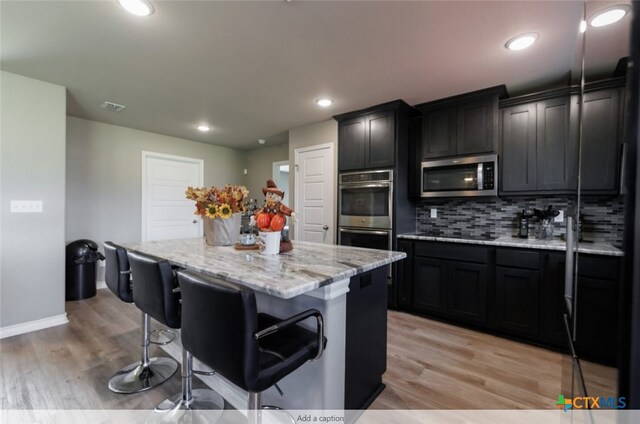 kitchen with a kitchen island, light hardwood / wood-style floors, a breakfast bar area, and appliances with stainless steel finishes