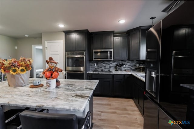 kitchen featuring appliances with stainless steel finishes, light wood-type flooring, backsplash, a breakfast bar, and hanging light fixtures