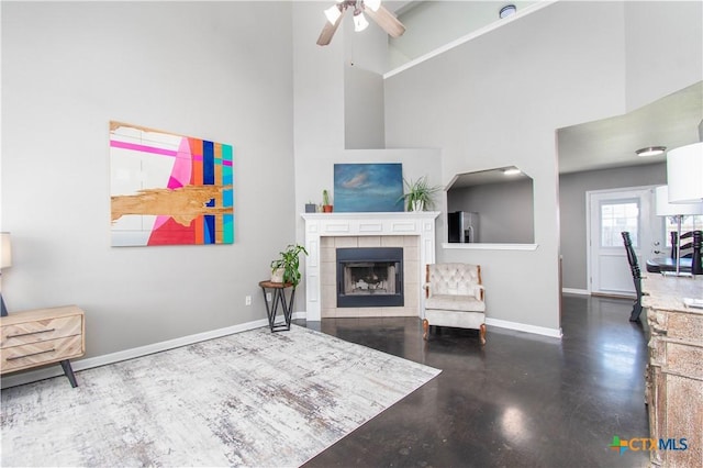 living room with a tile fireplace, a high ceiling, concrete floors, and baseboards