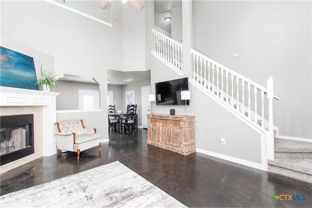 living area with concrete flooring, a tile fireplace, a ceiling fan, baseboards, and stairs